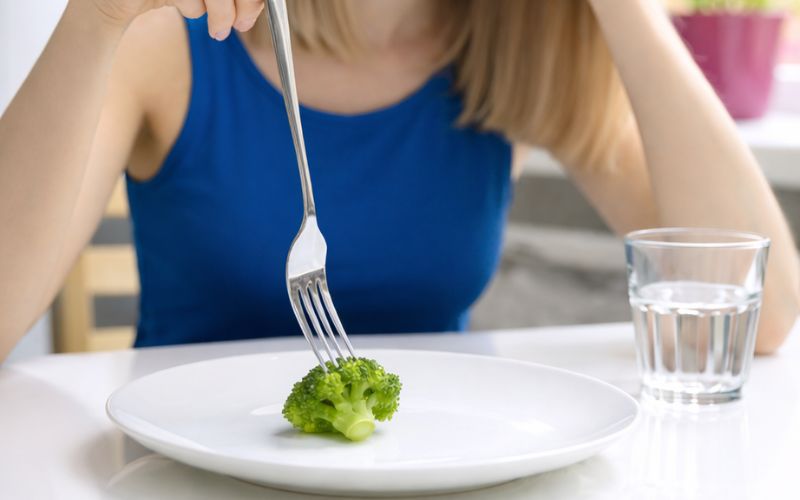 Woman playing with broccoli on plate using her fork.