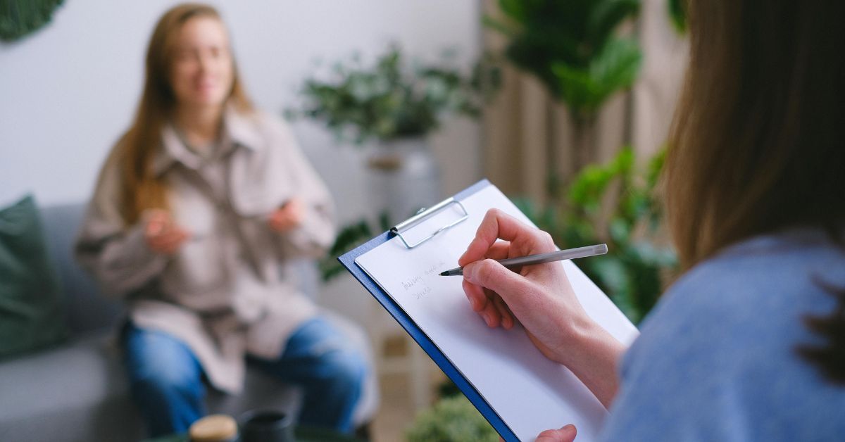 Therapist writing notes while client discusses concerns.