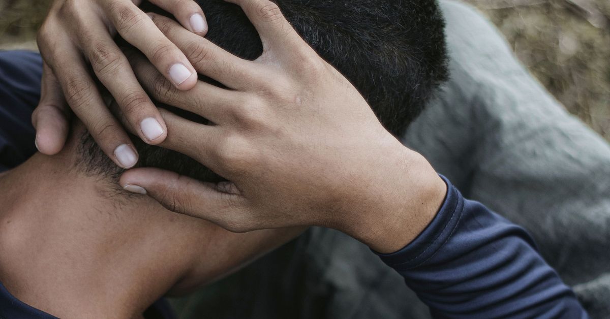 Man sitting with hands on neck, conveying a sense of worry and depression.